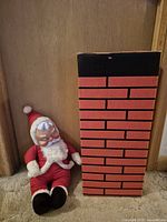 Santa figure seated beside brick-print chimney box