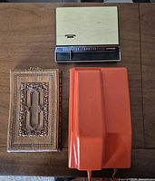 Three items laid out: brass-tone telephone directory, carved wooden notepad holder, orange wall phone base