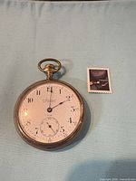 Front view of pocket watch beside postage stamp for scale