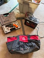 Group shot of all items: tool bag, charger, flare gun case open, gutter rake