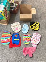 All eight dog garments laid out beside cardboard box on carpet