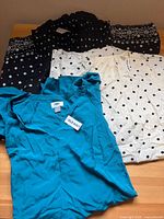 Three blouses laid out: teal, cream polka-dot, black floral