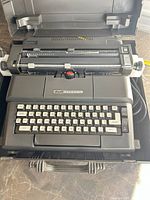 Top view of typewriter inside carrying case showing keyboard, carriage, power cord