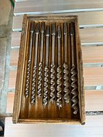 Open wooden box showing all ten spiral auger bits arranged by size