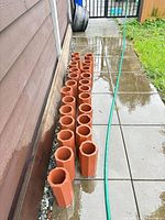 Row of 16 terracotta edging tubes along wall on patio