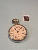 Front view of Westclox pocket watch beside postage stamp for scale