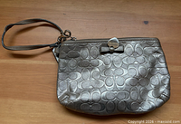 Front view of silver metallic Coach wristlet showing overall design and detachable wrist strap