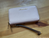 Front view of blush pebbled leather Michael Kors zip-around wristlet wallet with wrist strap visible