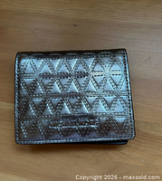 Front view of metallic bronze Michael Kors trifold wallet showing stitched triangle pattern and logo