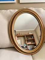 Front view of oval gold wood wall mirror on sofa