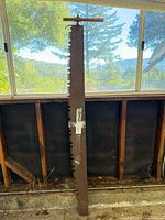 Full view of long crosscut saw blade leaning vertically, wood handle visible at top