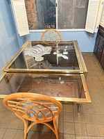 Overview of brass frame glass top table with both rattan chairs and glass bowl