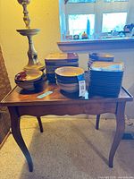 Stacked square ceramic plates and bowls on wooden table with brass-tone lamp