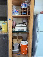 Full shelf view showing roaster oven, picnic basket, cooler, mixing container, disposable plates and cups