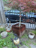 Square glazed planter with Japanese maple, three small pots, garden sprayer visible