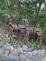 Both sheet metal deer sculptures standing on stone border in garden