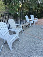 Three plastic Adirondack chairs and one wooden semicircle bench on patio