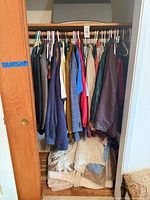 Closet view of assorted jackets, blazers, sweaters, shirts on hangers; throws and blanket on floor