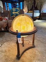 Illuminated globe on three-leg dark wood stand with power cord