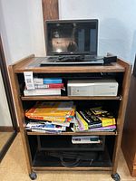 Full view of rolling AV cart with laptop on top shelf, books and CD changer in middle, paper and bag on bottom