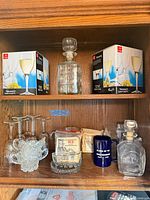 Cabinet shelf showing Toscana wine glass boxes, cut-glass decanter, pressed-glass cream & sugar, ceramic mug and additional decanter