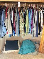 Full closet view of assorted tops on hangers, cushion and bedding on floor