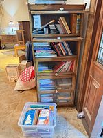 Full view of five-tier oak barrister bookcase with books inside and plastic bin of books on floor