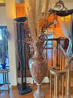 Full view of ornate red and gold ceramic floor vase with dried arrangement, next to lamp and stairs