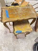 Two nesting tables stacked, showing tops with gilt and red motifs