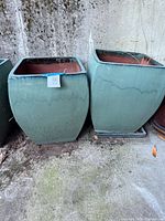 Two large square green-aqua planters with red interiors on matching saucers