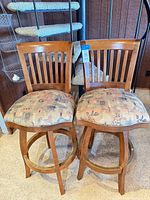 Front view of both wood bar stools showing upholstery, backs, and footrests