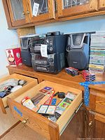 Full view of stereo system, one speaker, CD stack, cassette tapes, open drawer with accessories