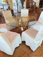 Full dining set view showing glass top on rattan base and six slipcovered chairs