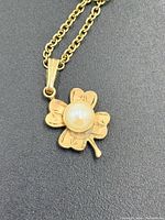 Close-up of clover pendant showing gold filled metal, engraved leaves, pearl center and bail