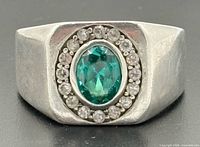 Front view of sterling silver signet ring showing oval emerald and surrounding clear stones