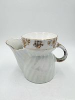 Front view of porcelain shaving scuttle showing handle, spout, spiral body and gilt floral rim