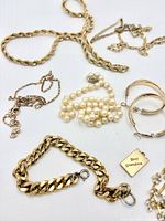 Overview of assorted gold-tone chains, bracelets, faux pearl bracelet, hoops, tag charm