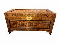 Front view of carved camphor wood chest showing brass latch and sailing ship panel