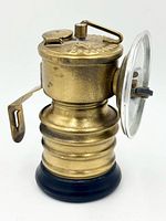 Side profile of brass carbide miners' lamp showing body, reflector and striker arm