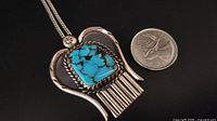 front view of pendant beside coin for scale showing turquoise stone and silver setting
