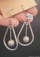 Front view of earrings showing teardrop shape, suspended balls, and hallmarked tag