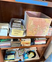 Bookshelf with plastic tub of cassette tapes, decorative box, stacks of CDs and some vinyl records