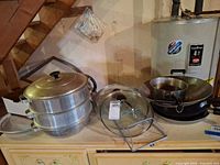 Group showing steamer pot set, glass lid, lid stand, wok on counter