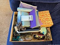 Overview of box containing assorted eyeglasses, sunglasses, multiple cases and cleaning cloths
