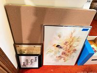 All items leaning: blank canvas, framed bird print, two smaller framed prints