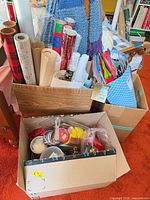 Two boxes containing wrapping paper rolls, gift bags, ribbons and bows