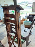 Upper section of wooden ladder showing top platform, hinge hardware, paint splatters