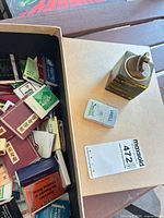 Open box showing numerous matchbooks, wood block table lighter and two matchboxes on lid