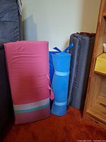 Group shot of pink foam mattress, blue rolled mat, blue Aerobed bag, grey rolled pad