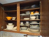 Cabinet view showing stacked plates, mugs, bowls, lidded casseroles, glass bowls, yellow ramekins